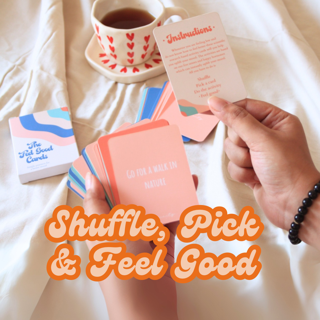 Person holding a card from a deck of feel good cards with a cup of tea and additional cards on a light surface.